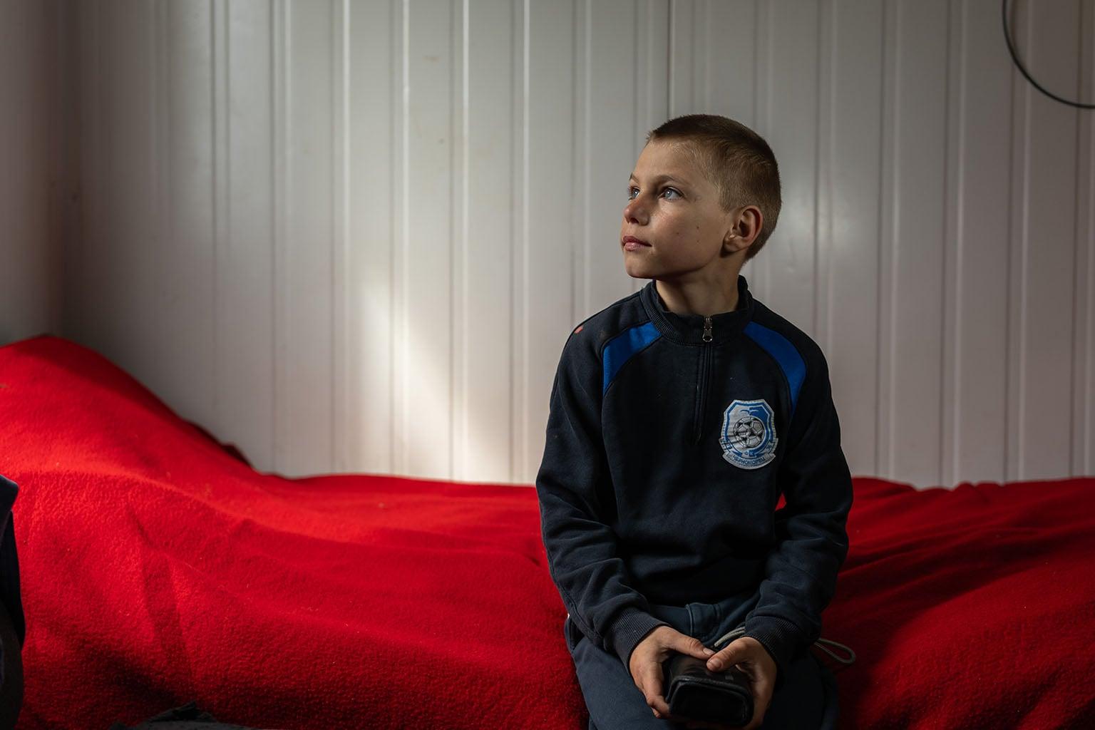 Tolya (9) op bed in noodwoning