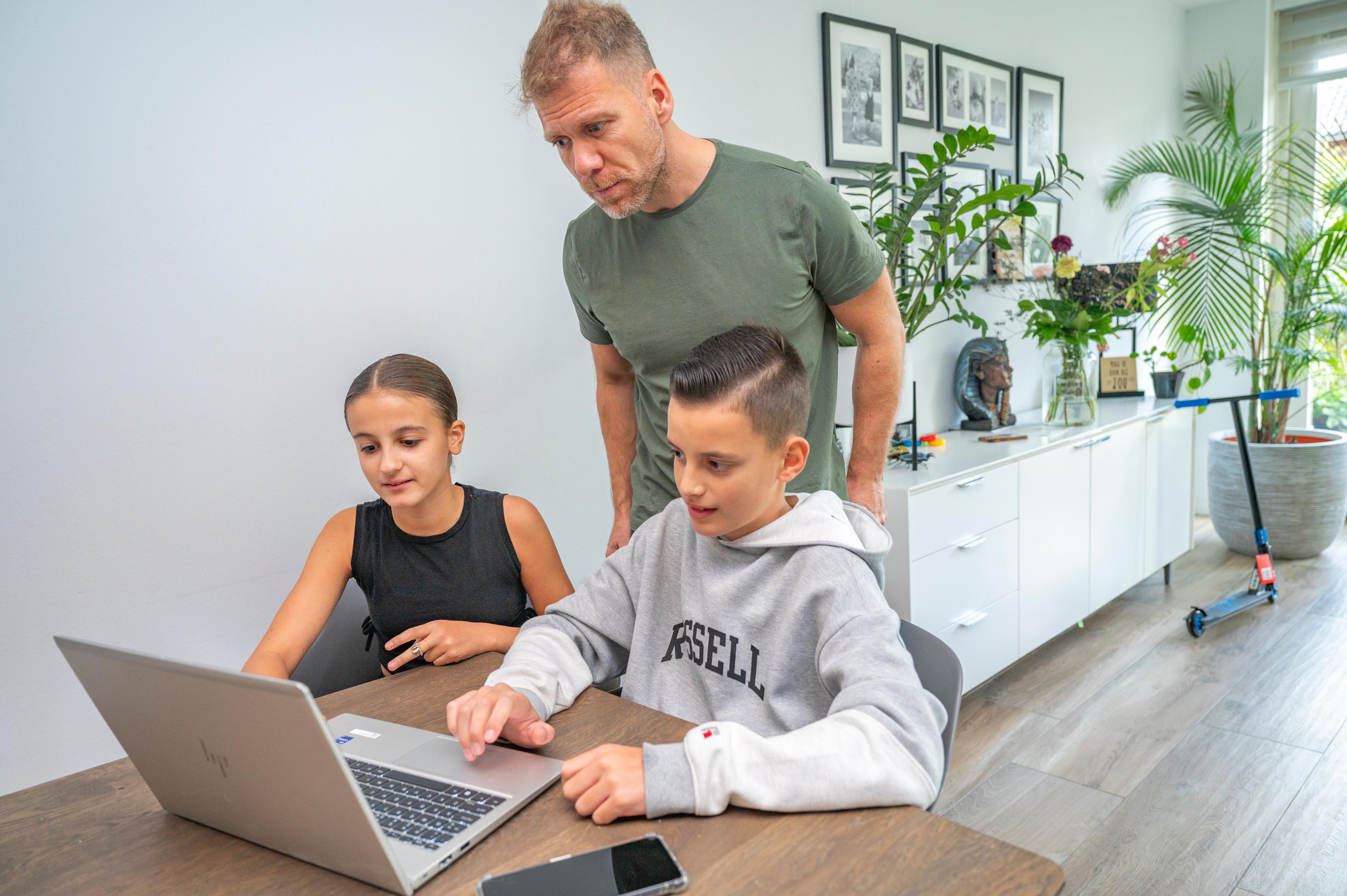 Vader kijkt met twee kinderen mee op een laptop
