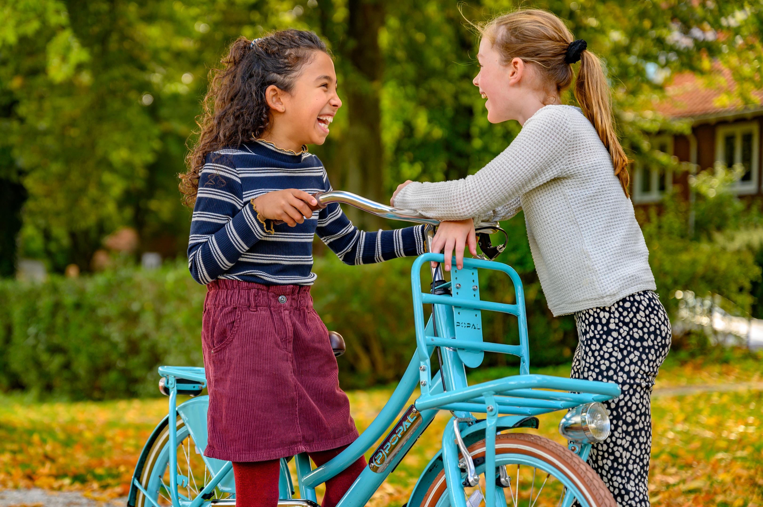 Foto van twee meisjes lachend bij een blauwe fiets.