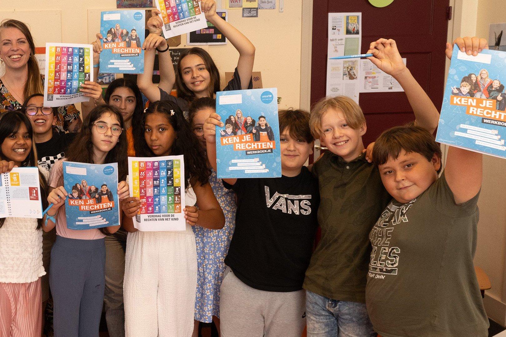 Kinderen en leerkracht houden lesmateriaal omhoog