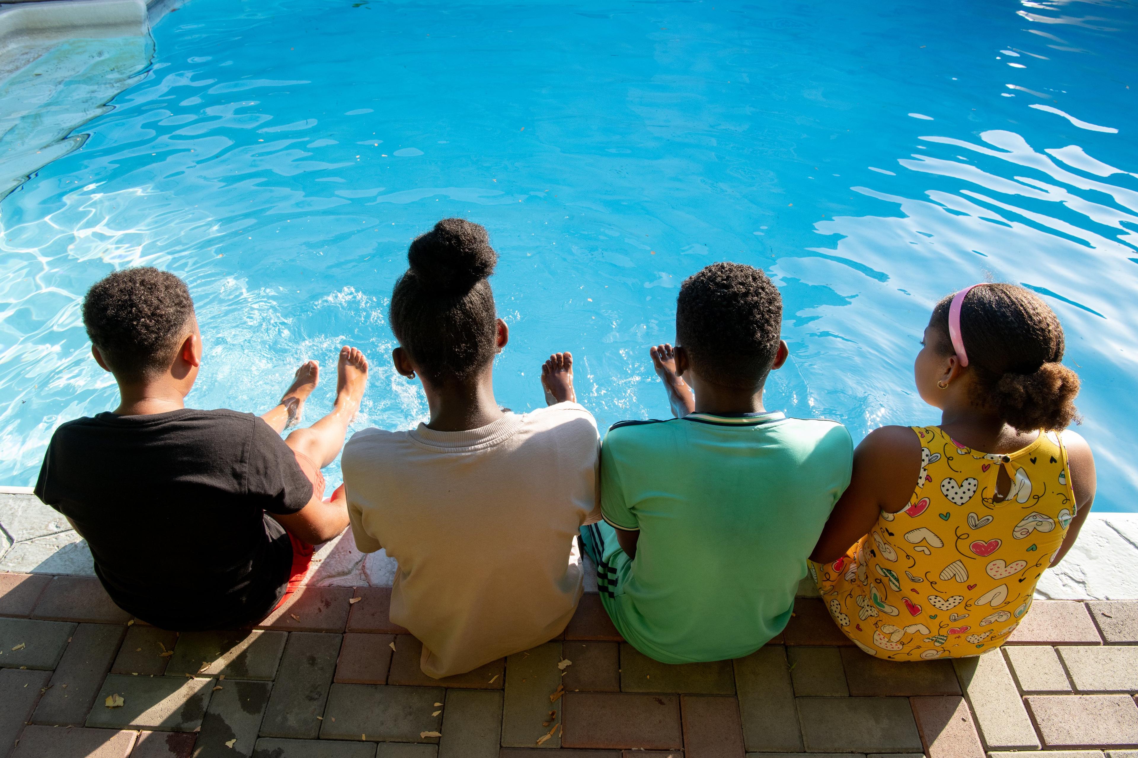 vier jongeren uit Caribisch Nederland zitten met rug naar de camera bij het water