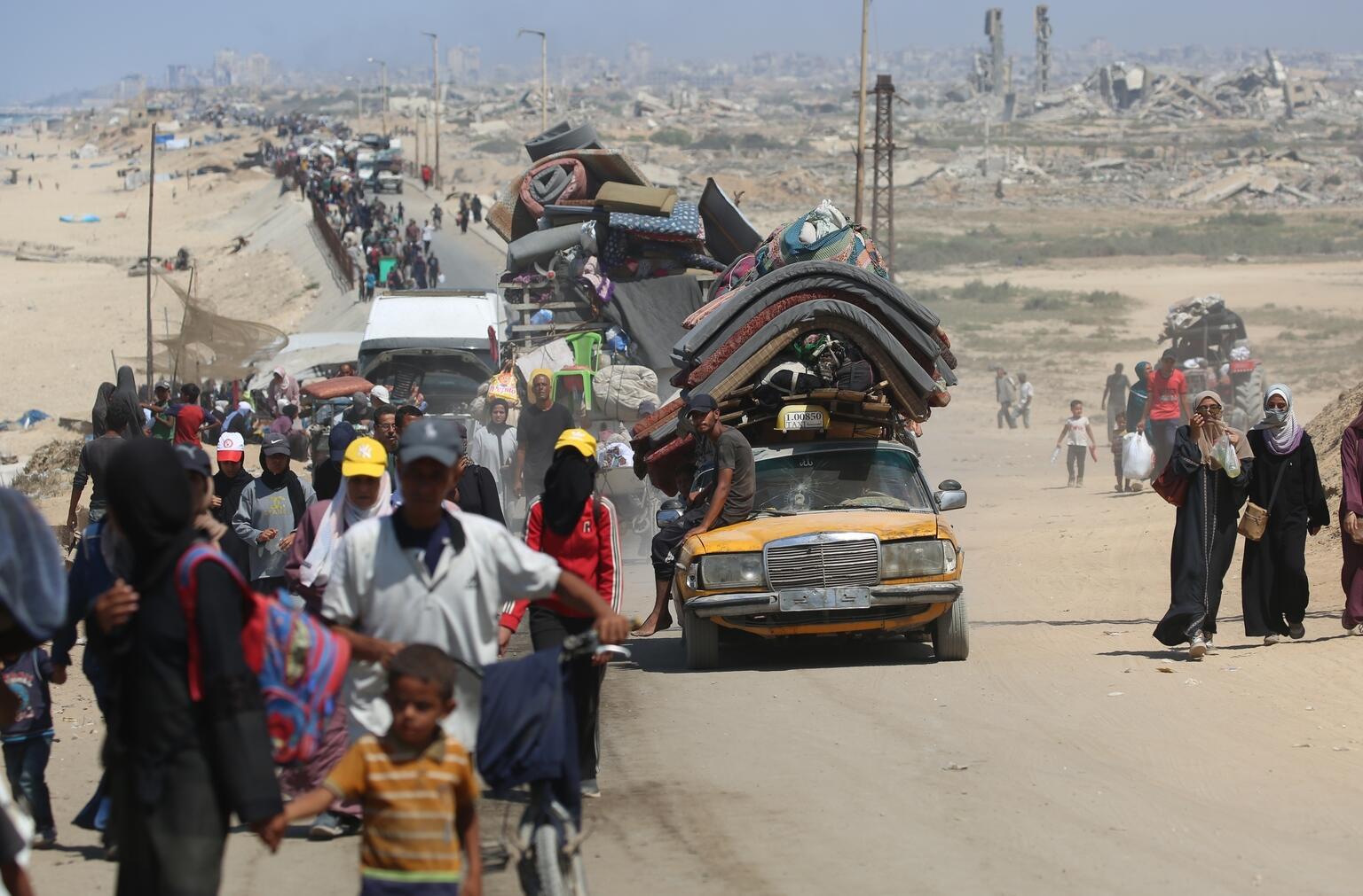 Palestijnse families in Gaza op straat zijn op de vlucht vanaf het Noorden. In het midden zie je een bepakte auto, er omheen veel lopende vrouwen, mannen en kinderen.