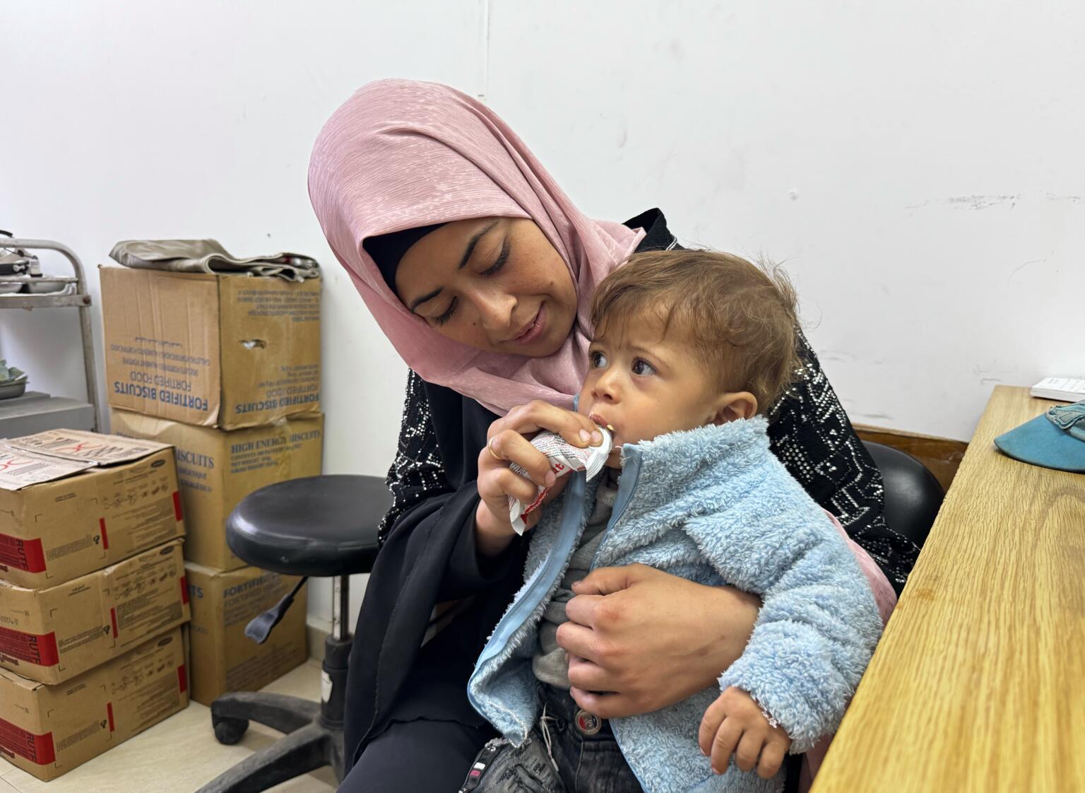 Een kind in Gaza zit bij moeder op schoot en krijgt therapeutische voeding in een door UNICEF-gesteund voedingscentrum.