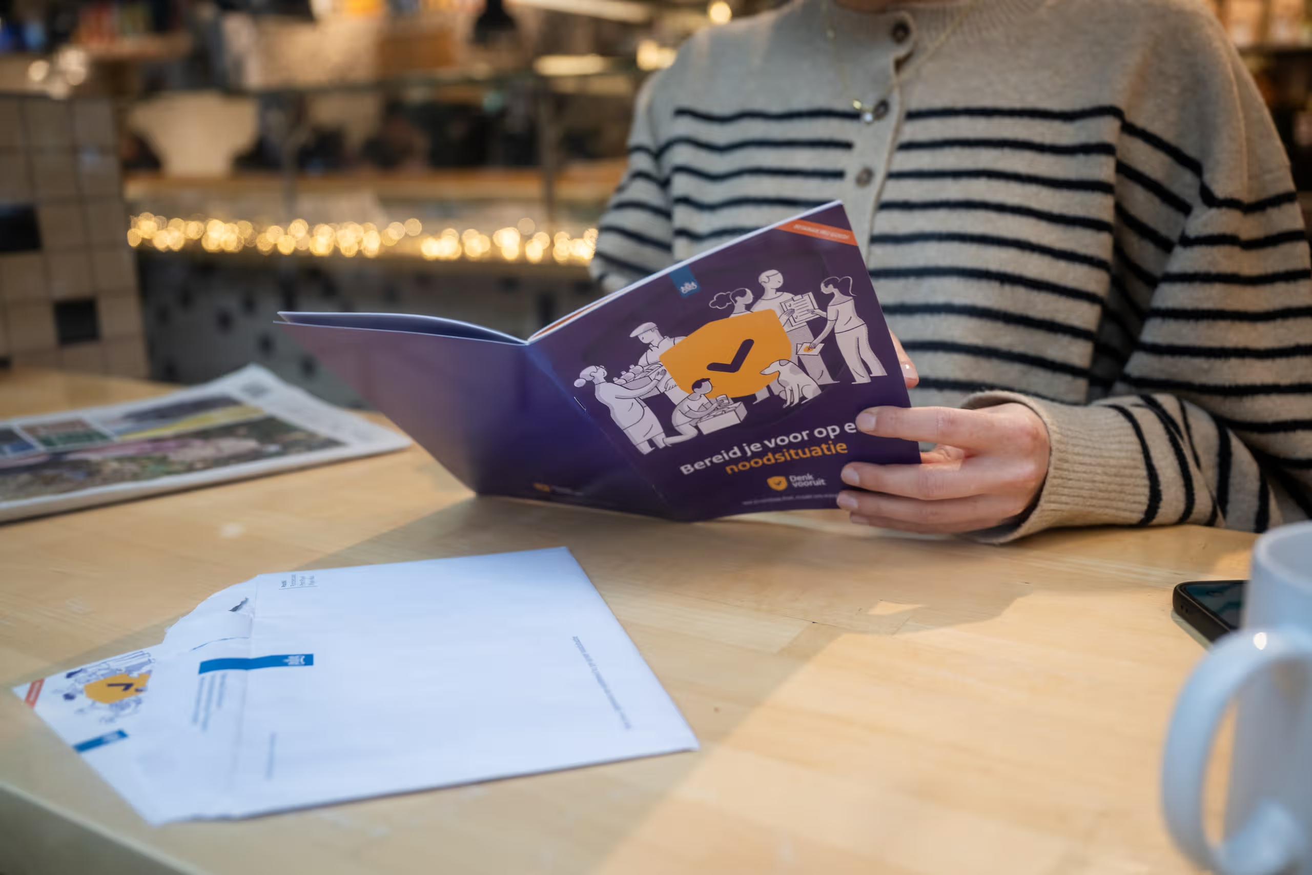 Foto van iemand die het informatieboekje van de Denk Vooruit campagne leest