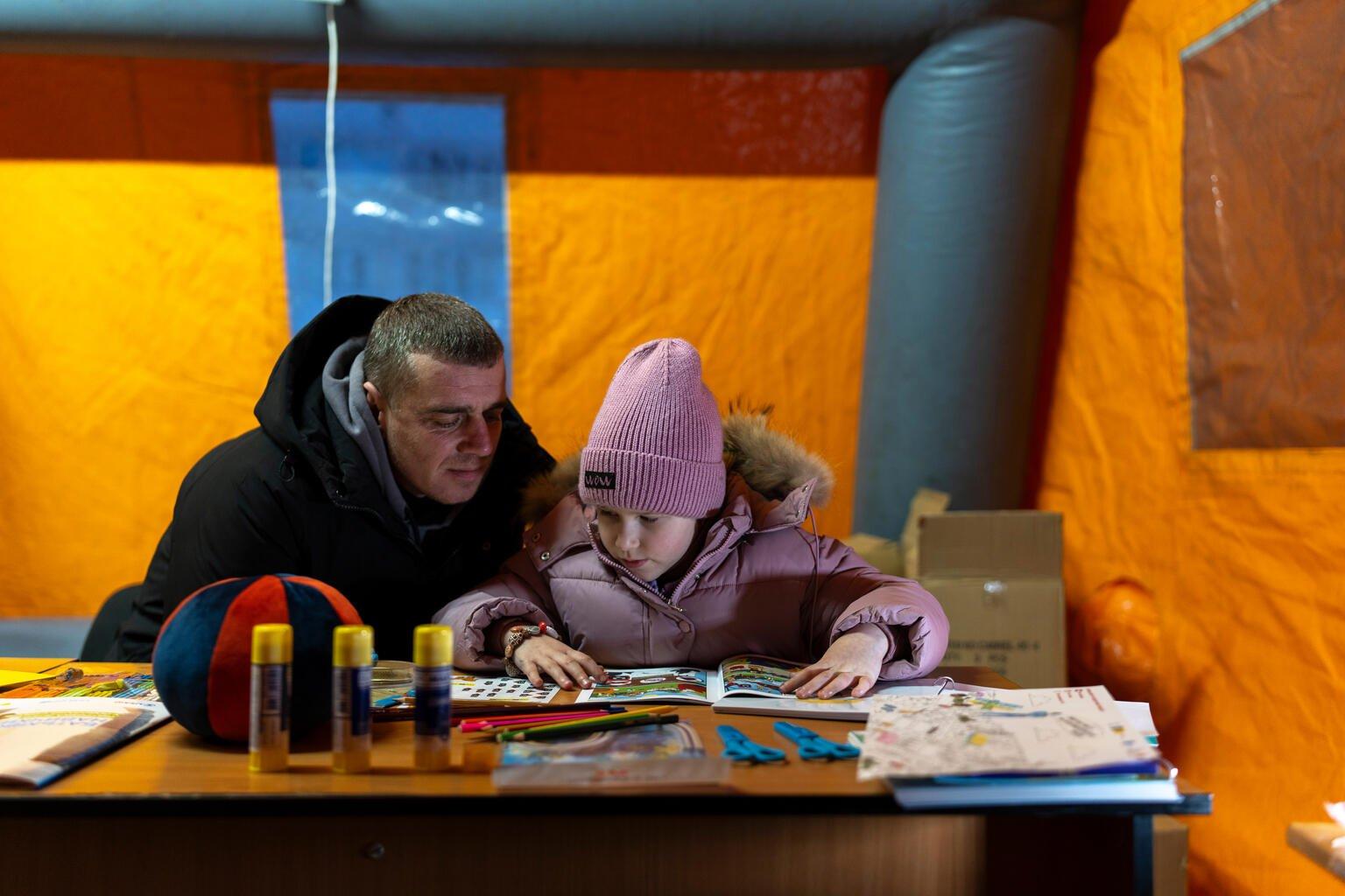 Een vader en een kind zitten te kleuren in een verwarmde mobiele tent.