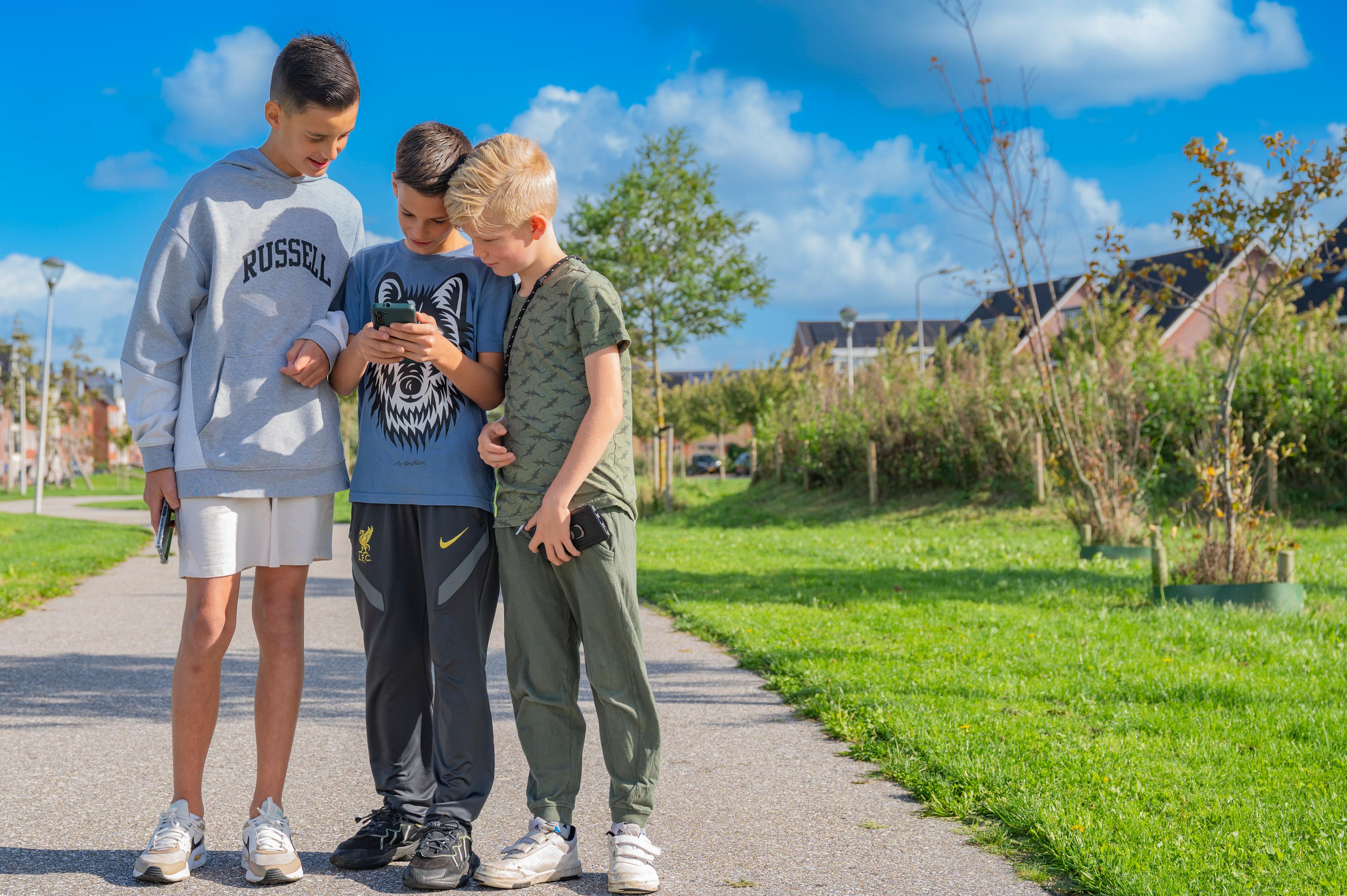 drie-jongens-kijken-buiten-naar-een-telefoon