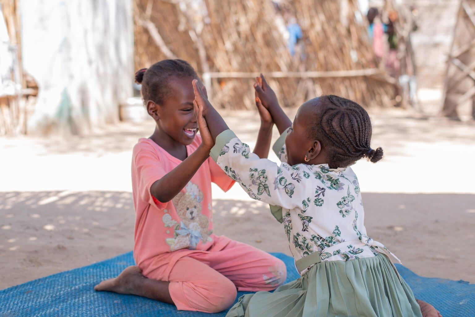 Twee meisjes high-fiven terwijl ze op de grond zitten te spelen in Soedan.