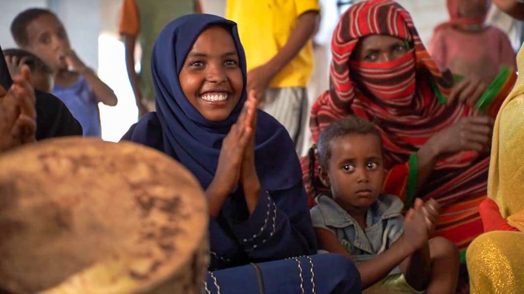 Een lachend meisje in Soedan zit klappend tussen andere kinderen te spelen.