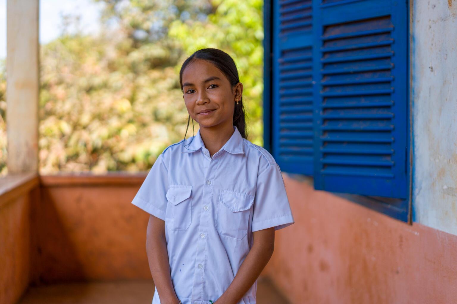 Meisje poseert voor haar school in Cambodja