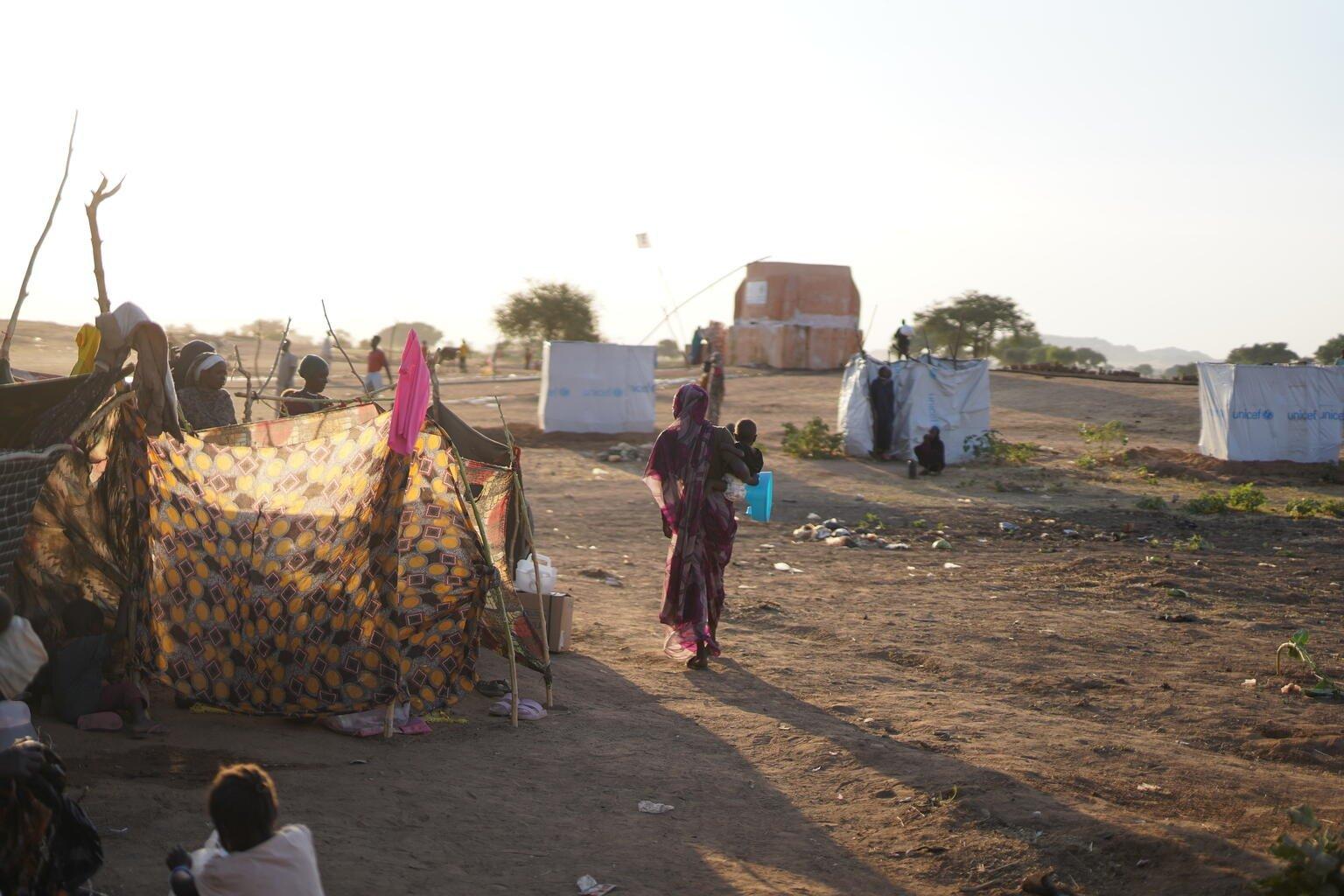 Een moeder staat midden in een vluchtelingenkamp in Soedan met haar rug naar de camera toe.