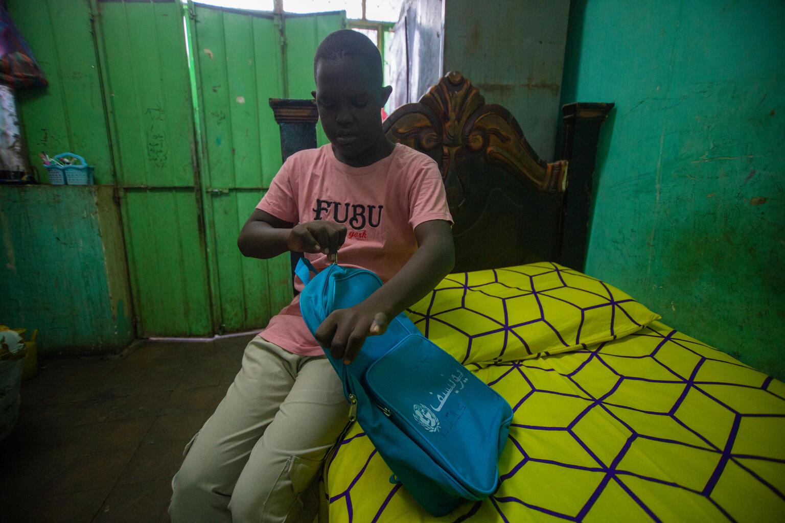 Jongen in Soedan pakt zijn schooltas tas in op zijn bed om naar een kindvriendelijke ruimte te gaan.