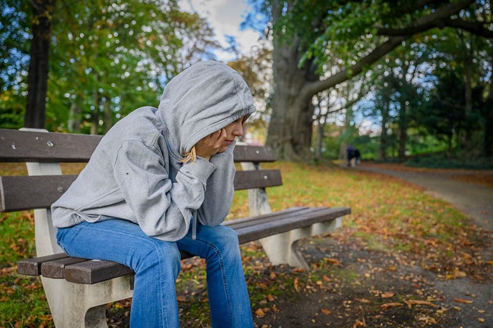 Meisje met een hoody zit in een park op een bankje.