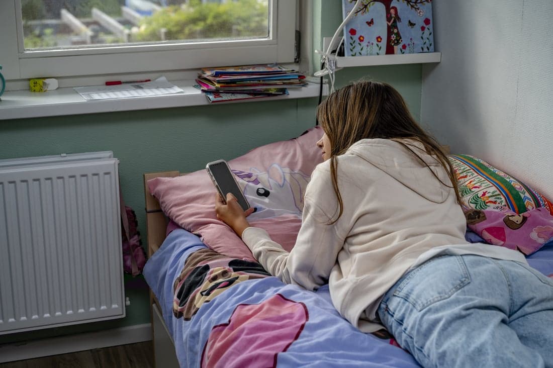 Meisje zit in haar kamer en gebruikt haar mobiele telefoon.