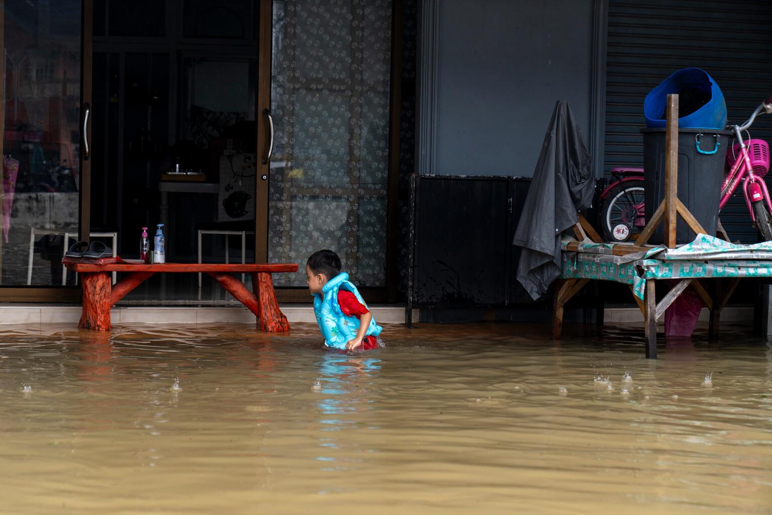 Een foto van een kind in Thailand in een overstroomd huis.