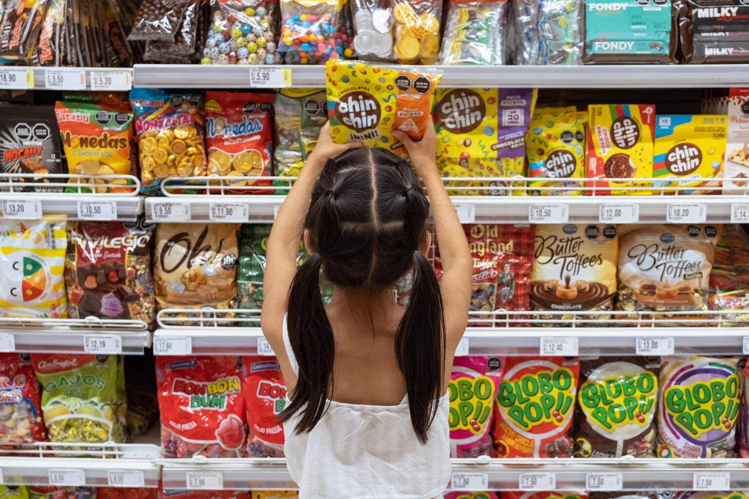 Meisje staat voor een schap in de supermarkt vol snoep en snacks