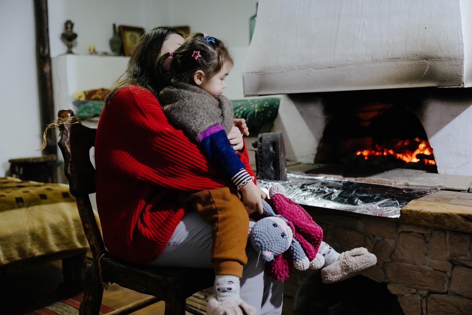 moeder met kind op schoot bij houtkachel in Oekraïne